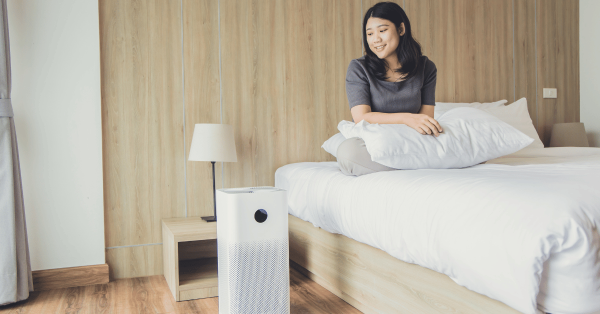 mulher sentada na cama olhando pro purificador de ar